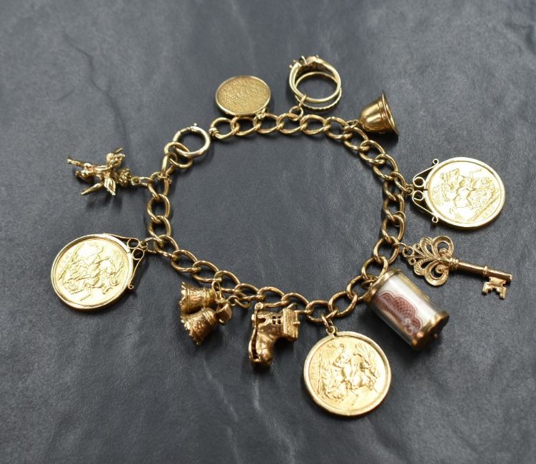 A 9ct gold curb link bracelet, having three sovereigns in removable mounts and a further eight charms including a key, a police hat and a 10 shillings note, 63.5g