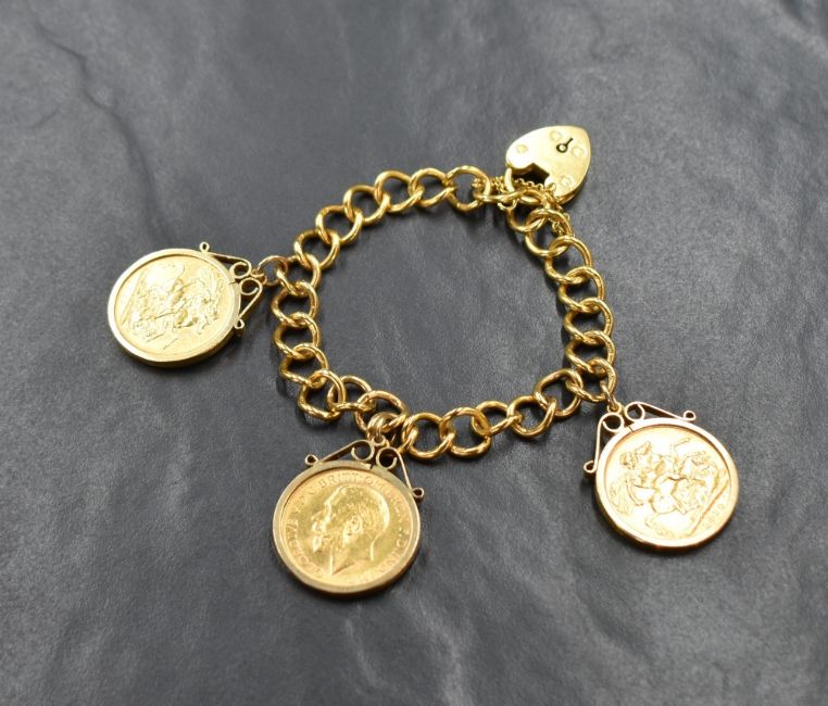 A 22ct gold curb link bracelet, having three sovereign coins in removable mounts, along with a heart padlock and safety chain, 55.9g